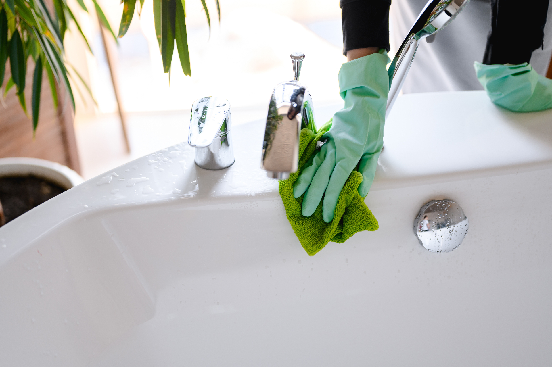 Cleaner wiping down a spotless white bathtub in a residential bathroom