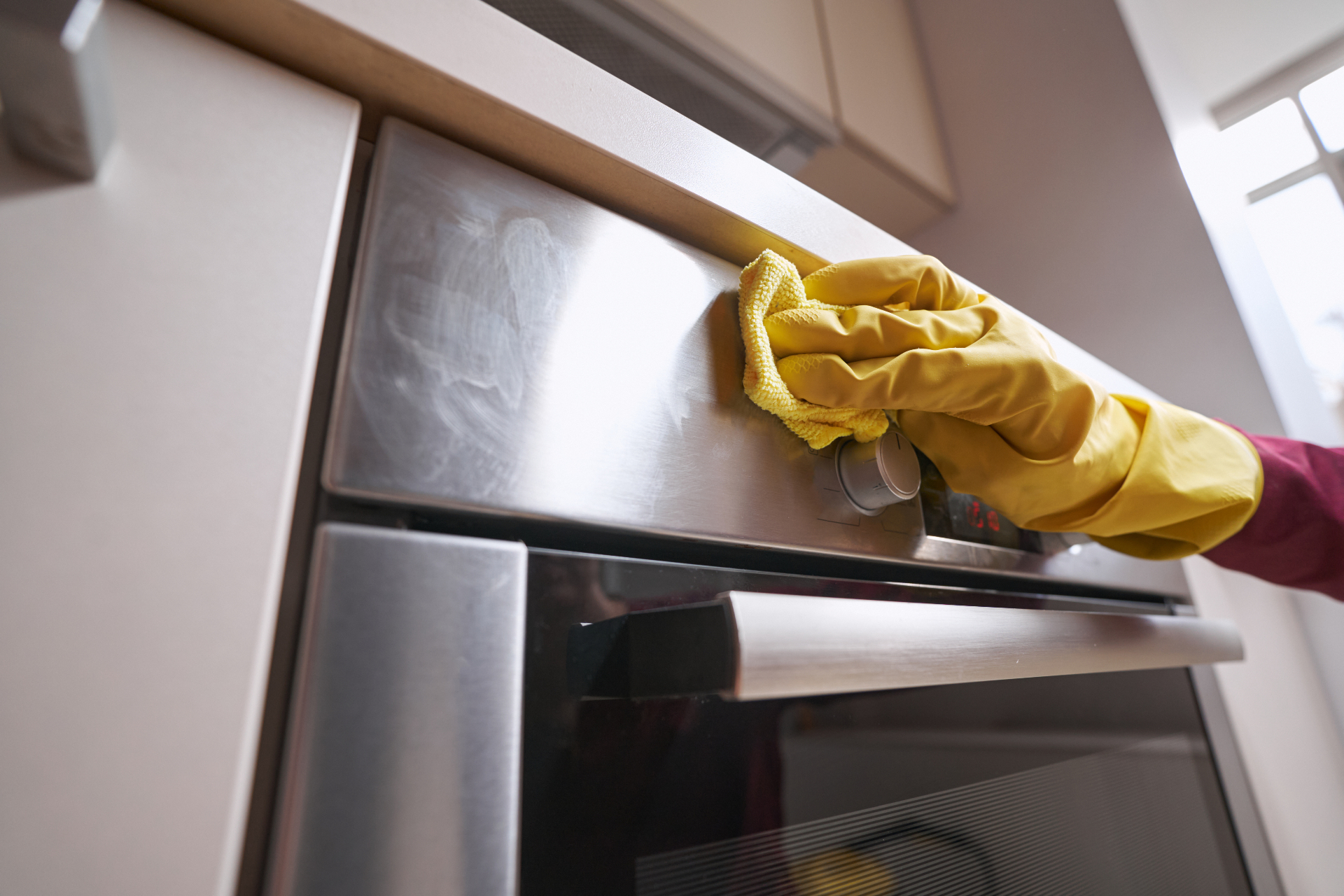 Cleaner polishing a stainless steel oven during a domestic deep clean