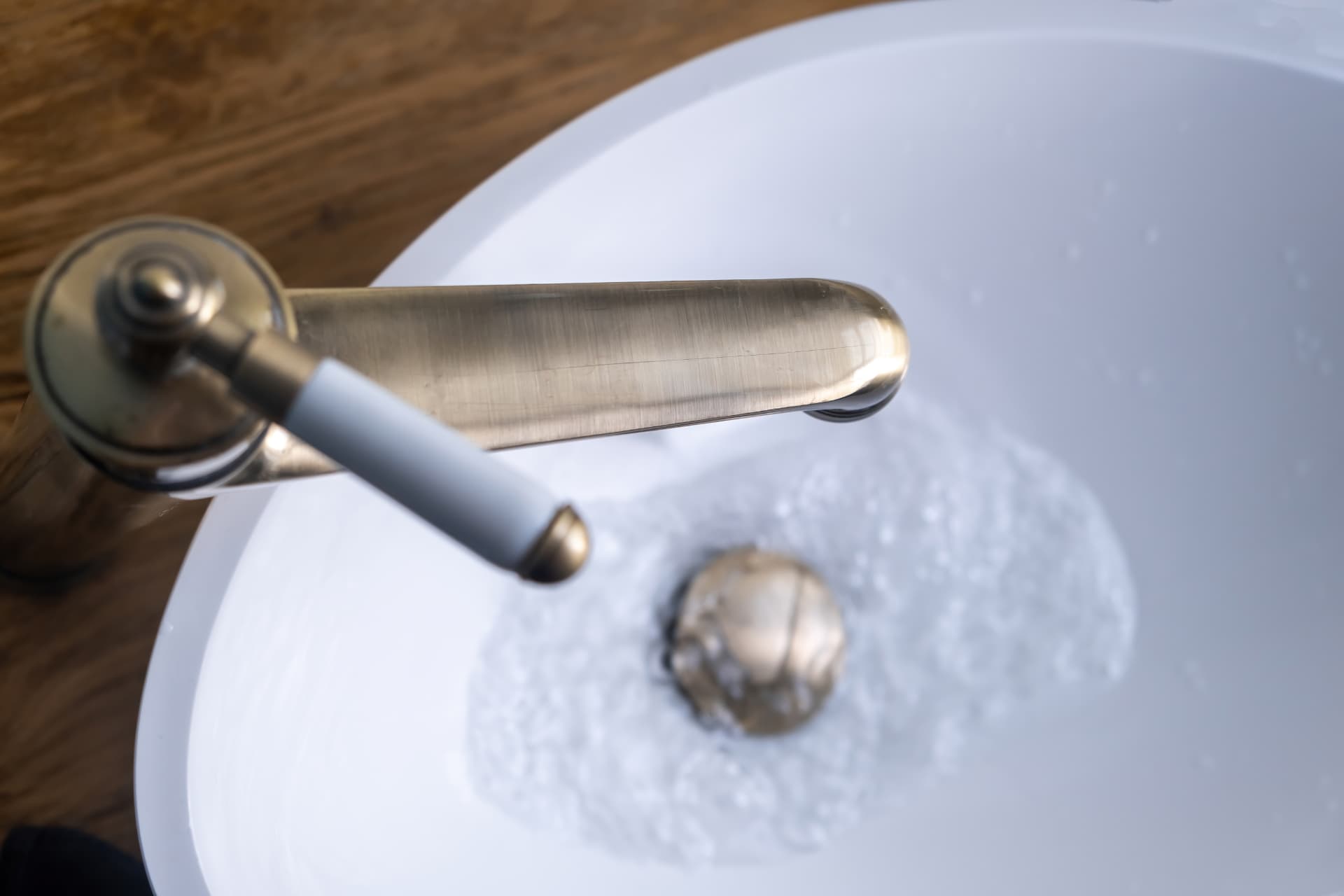 Close up of a brushed metal bathroom tap running water into a white basin